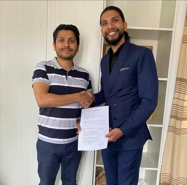 Samir shaking hands and holding a signed agreement